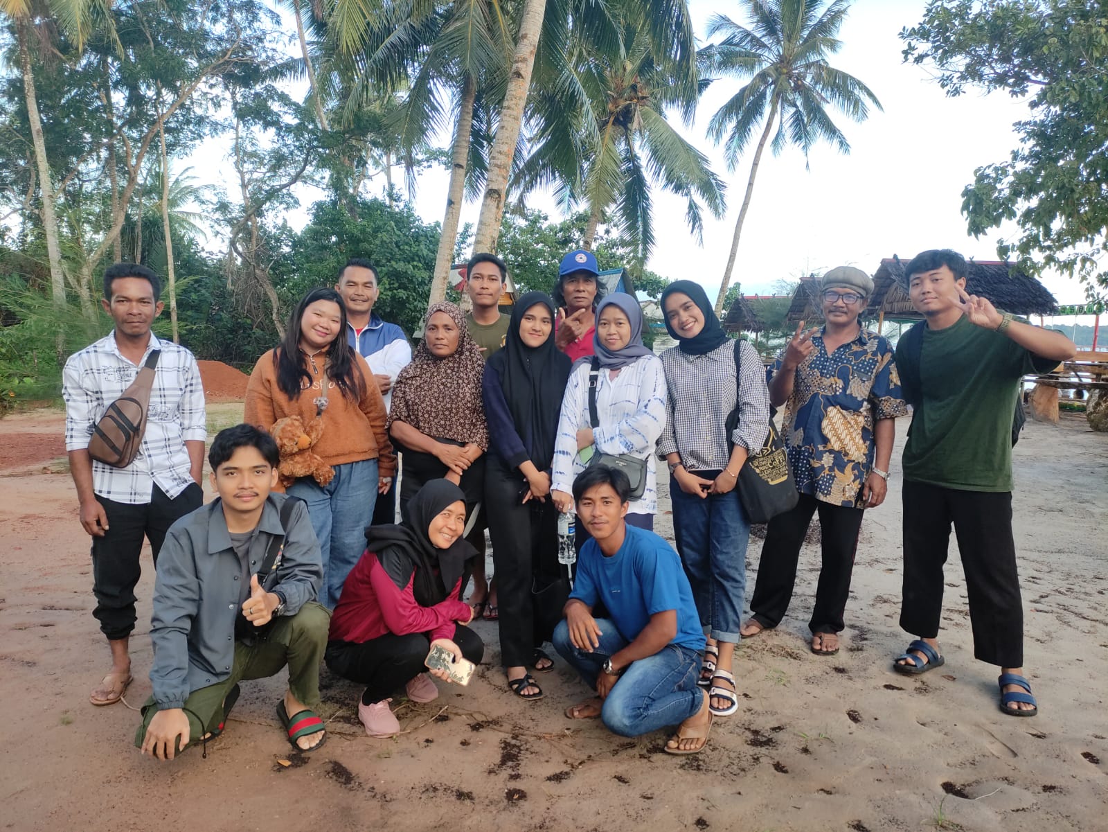 A group picture between CarbonEthics educators and local farmers and villagers on the beach with a lot of coconut trees in the background. Dompak island, blue carbon education, Indonesia coastal communities. CarbonEthics Indonesia