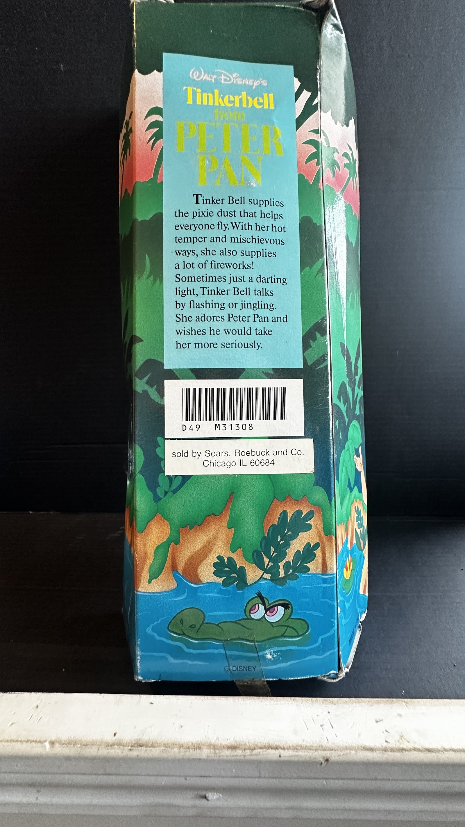 Teal printed cardboard box panel featuring Tinker Bell character biography text and Tick-Tock Crocodile illustration, with Sears distribution sticker and Disney copyright marking, showing edge wear and corner creasing