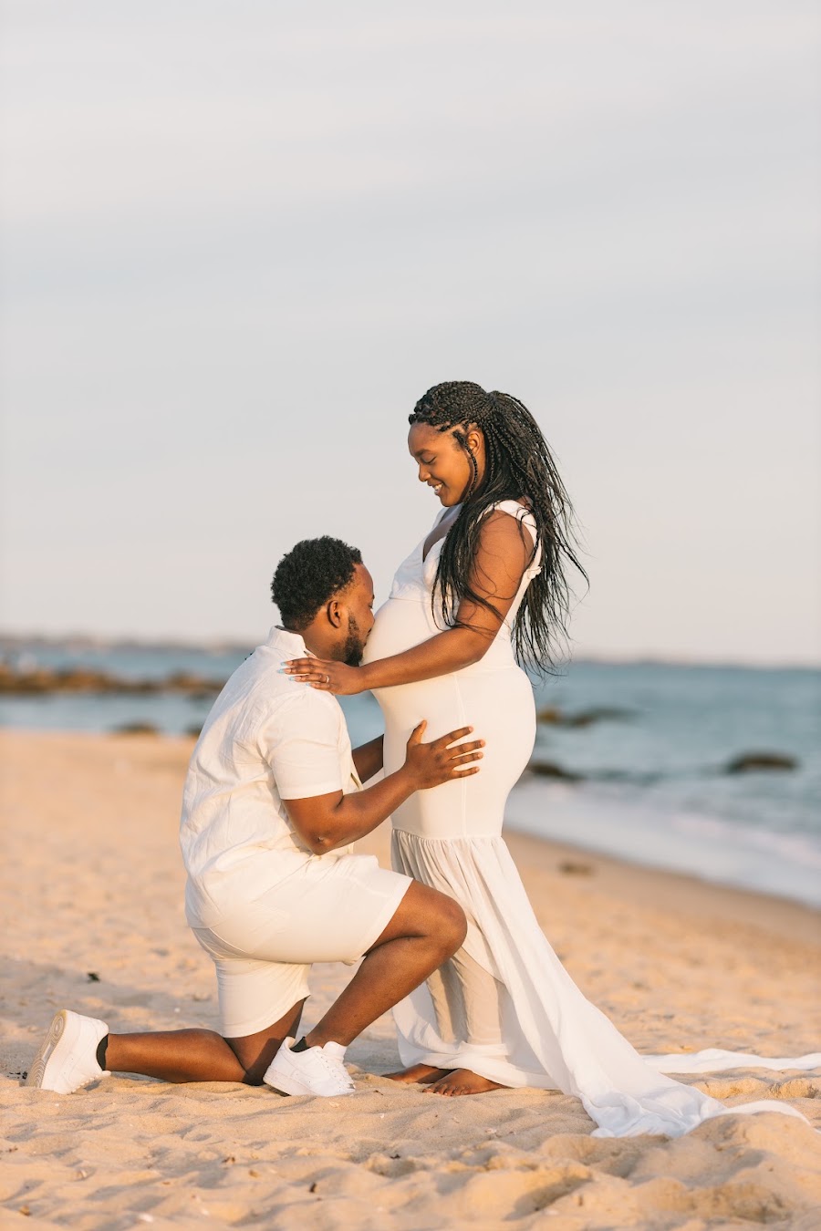 Partner kneeling to kiss the bump — beach maternity session