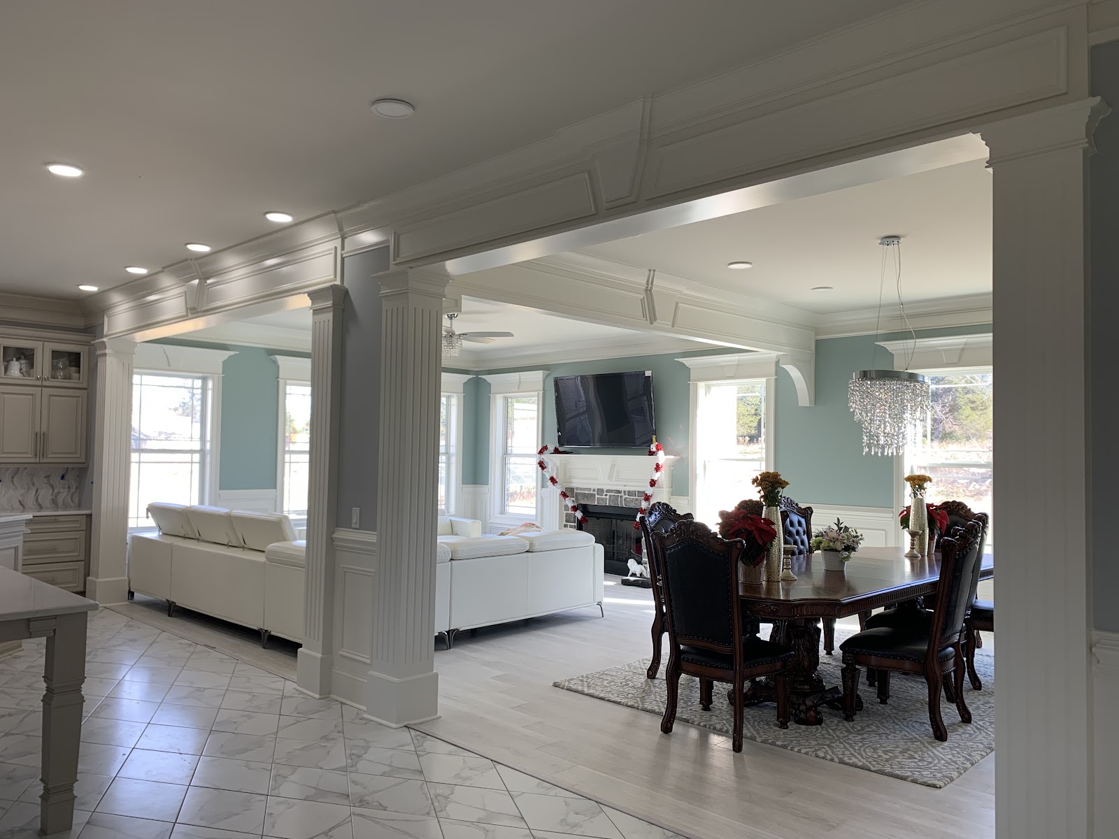 Open-concept interior showing a dining area with a dark wood table and a living area with white sofas, separated by white pillars.