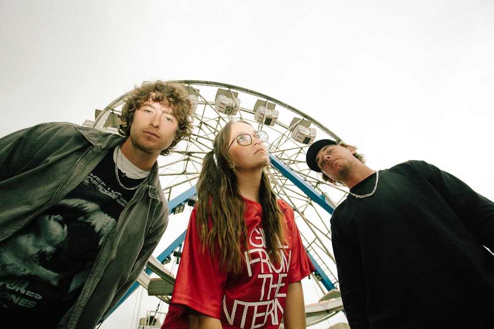 The three members of the Los Angeles rock band Out in Front pose in front of a ferris wheel