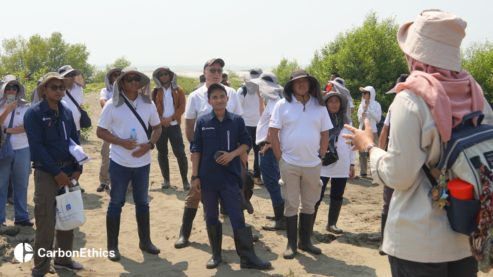CarbonEthics CEO Bimo Soewadji, standing in the center, alongside Telin representatives and other participants, attentively listening to a speaker during the mangrove planting event at the restoration site in Tanjungpakis, Karawang, West Java.