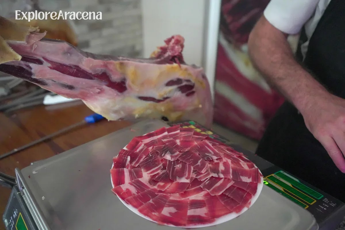 Thin slices of jamón arranged on a plate beside the cured ham leg from which they were cut.