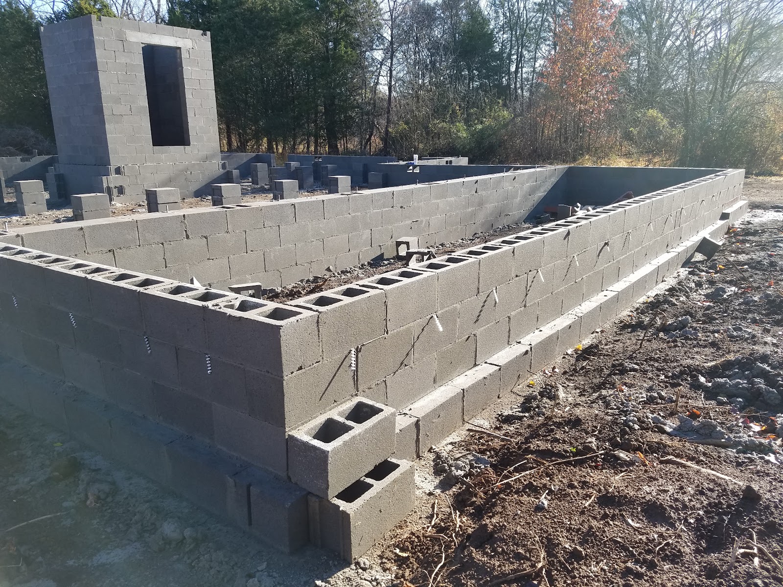 Concrete block foundation and a taller storm shelter structure under construction on a residential site in a rural area.