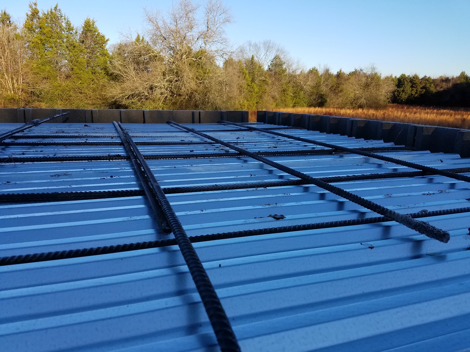 Rebar grid laid across a corrugated metal roof deck, with a rural landscape in the background.