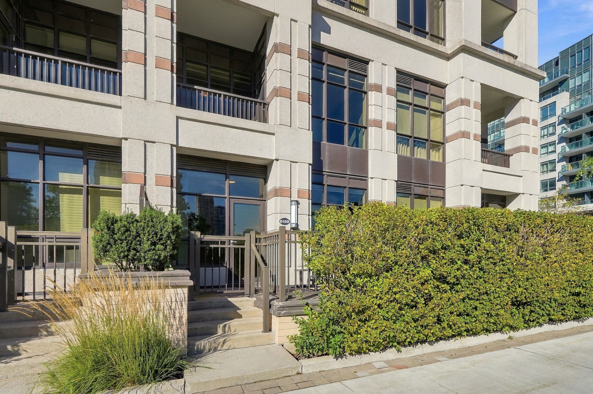 The private street-level front door of unit D108, up a few steps behind a hedge