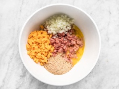 Tiếp đó cho thịt bò bằm, hành tây, phô mai, hỗn hợp breadcrumbs cùng trứng vào một tô lớn hơn và trộn thật đều với nhau. Sau đó cho thịt vào thố nướng và tạo thành hình chữ nhật. Nước sốt: trộn đều tương cà, đường nâu, mù tạt vàng cùng sốt Worcestershire với nhau rồi rưới lên bề mặt thịt, dàn cho trải khắp tất cả mọi chỗ. Cho khay thịt vào lò nướng 50 - 55 phút là thịt chín. Lấy thịt ra cho nguội một chút rồi cắt thành từng miếng vừa ăn.
