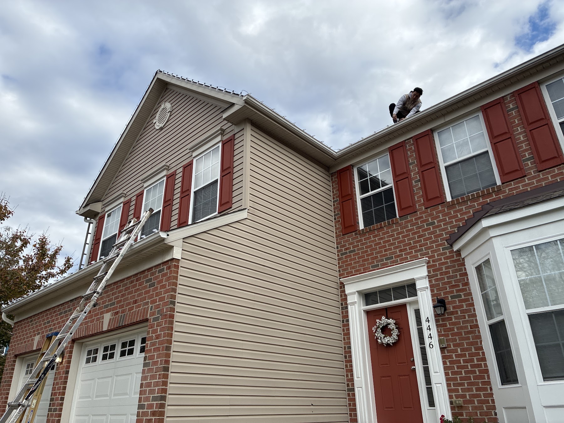 Holiday Lights DMV installer securing lights along a roof edge with ladders in place