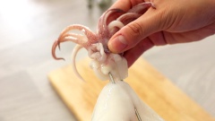 Đến công đoạn làm cho mực biến hình và bung nở khổng lồ rồi. Dùng dao sắc cắt 2 bên lá mực, mỗi bên cắt khoảng 4-5 đường, nhớ cắt sâu vào 1/2 lá để mực được bung hết cỡ khi chiên. Tiếp đến chuẩn bị que xiên dài để cố định thân và đầu mực, dùng que inox hoặc que tre đều được. Nếu dùng que tre, để không bị cháy khi chiên, bạn chỉ cần ngâm que vào nước trước 30 phút. Khi xiên, luồn que vào lá mực giống như kiểu đang dùng kim may đồ để xiên mực được chắc chắn.