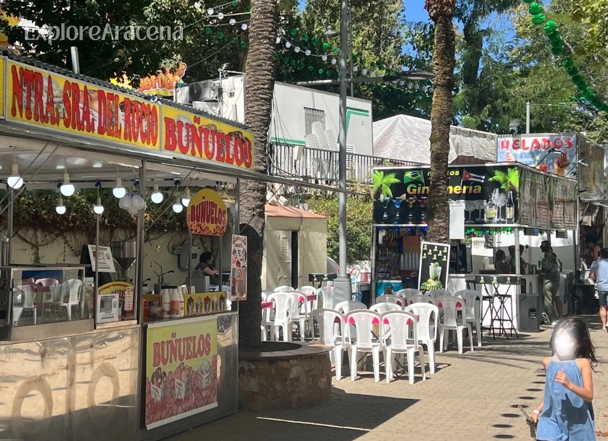 Daytime Feria de Aracena grounds with a buñuelos stand, ice cream kiosk and outdoor seating.