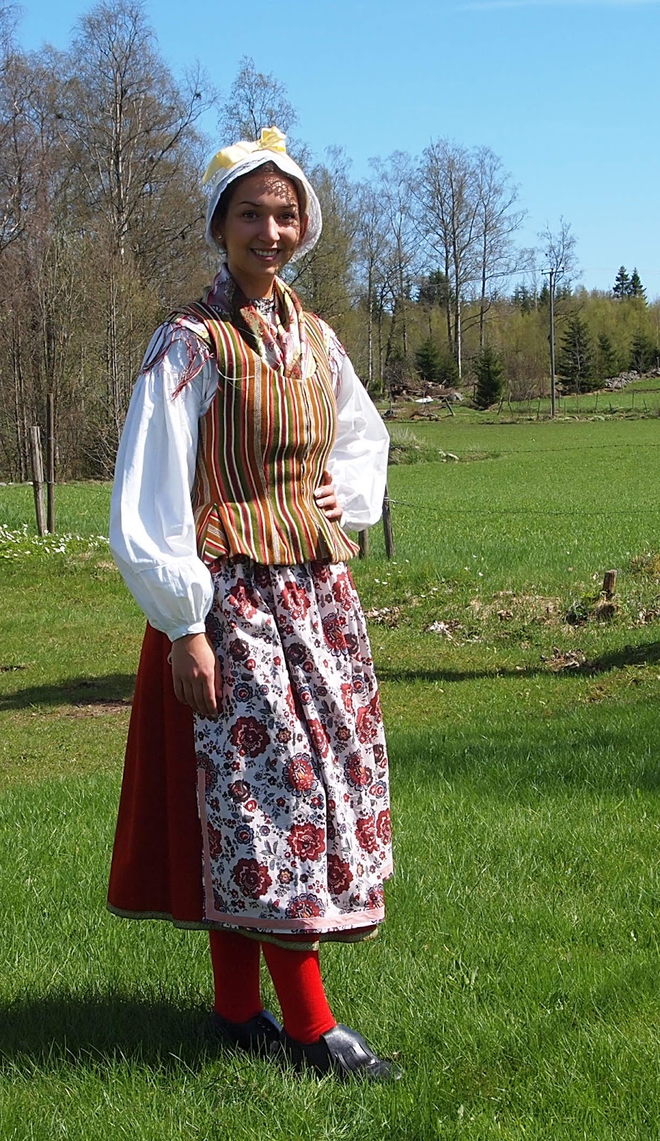 Småland, Västbo. Isabell bär livstycke i den så kallade Reftelerandningen, kattunförkläde som är kantat med band, röd kjol med g.