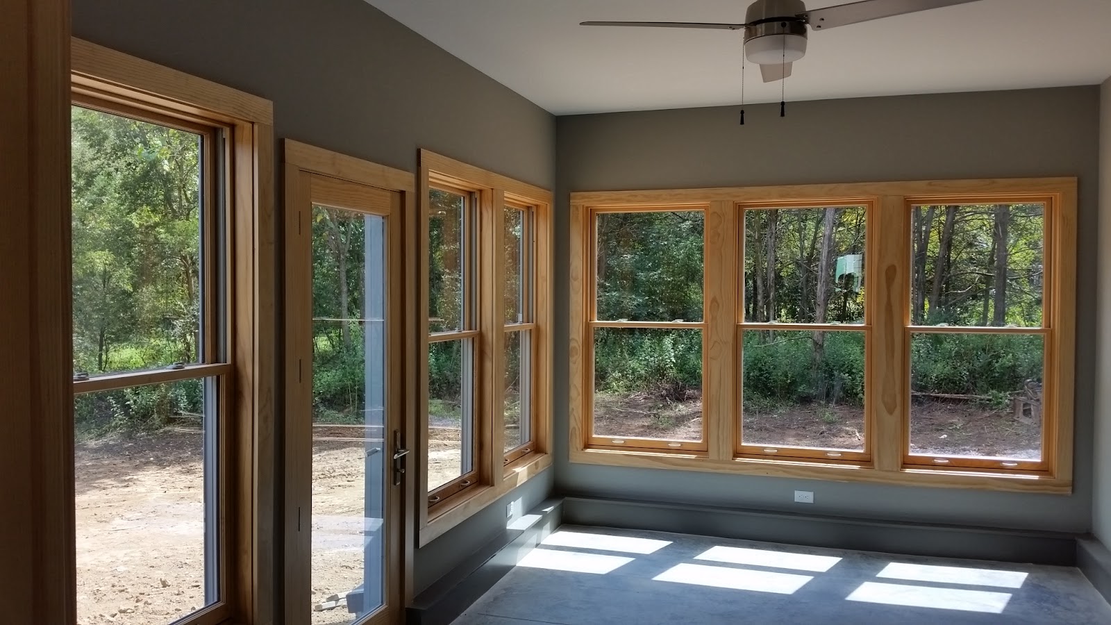 Interior room with grey walls and multiple large windows and a door, all featuring light wood frames, looking out onto a wooded area in East Tennessee.