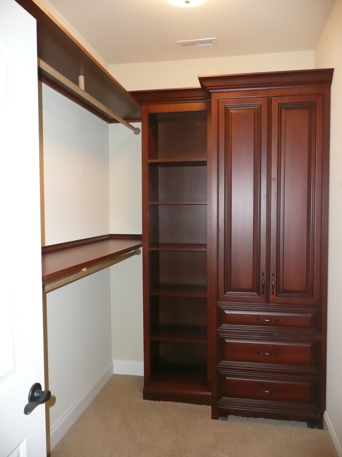 A walk-in closet with dark wood built-in cabinetry including open shelves, drawers, and a wardrobe.