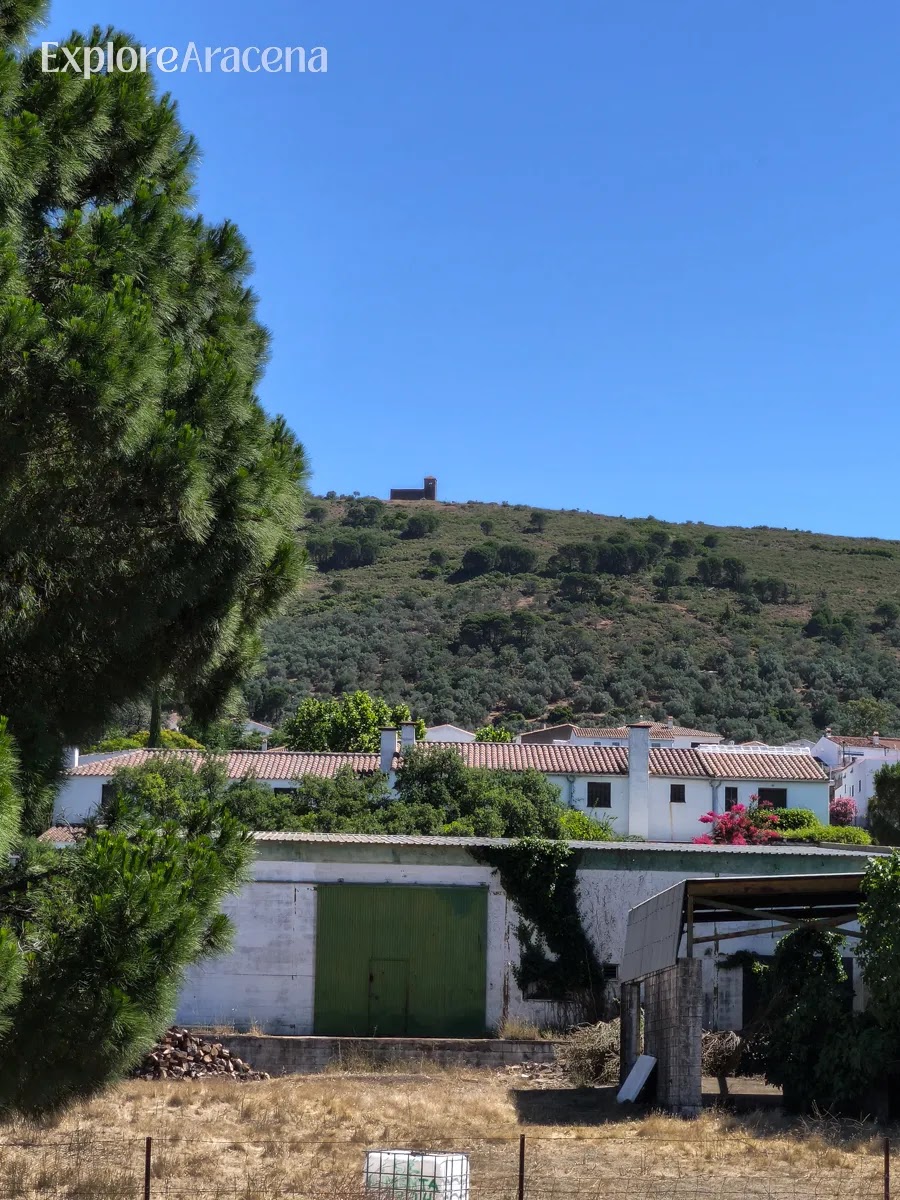 View across the Sierra de Aracena with rolling hills, whitewashed houses, and a hilltop church near the Martes Santos distillery.