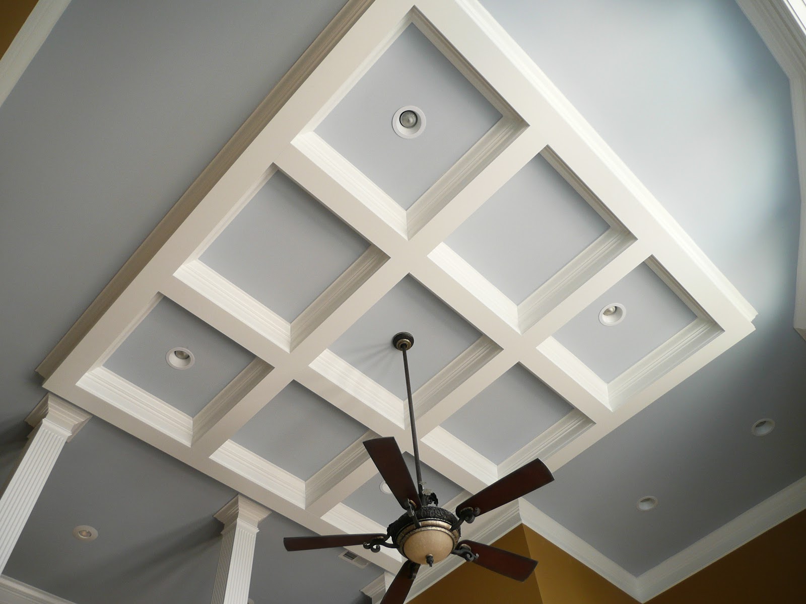 A white coffered ceiling with light blue panels, recessed lighting, and a dark ceiling fan.