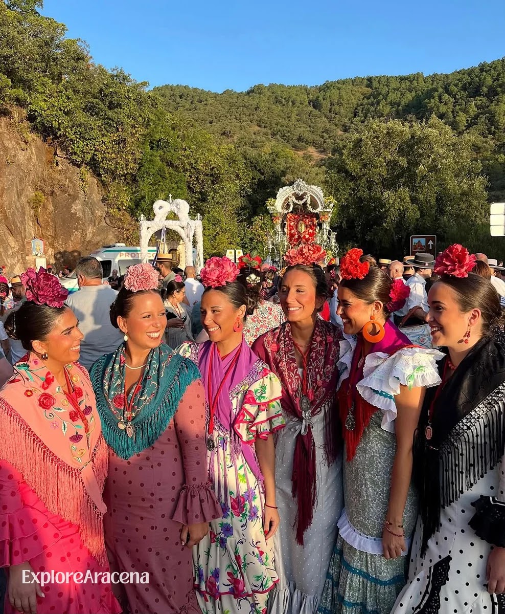 Women wearing colourful flamenca dresses with the silver shrine visible behind them at the romería