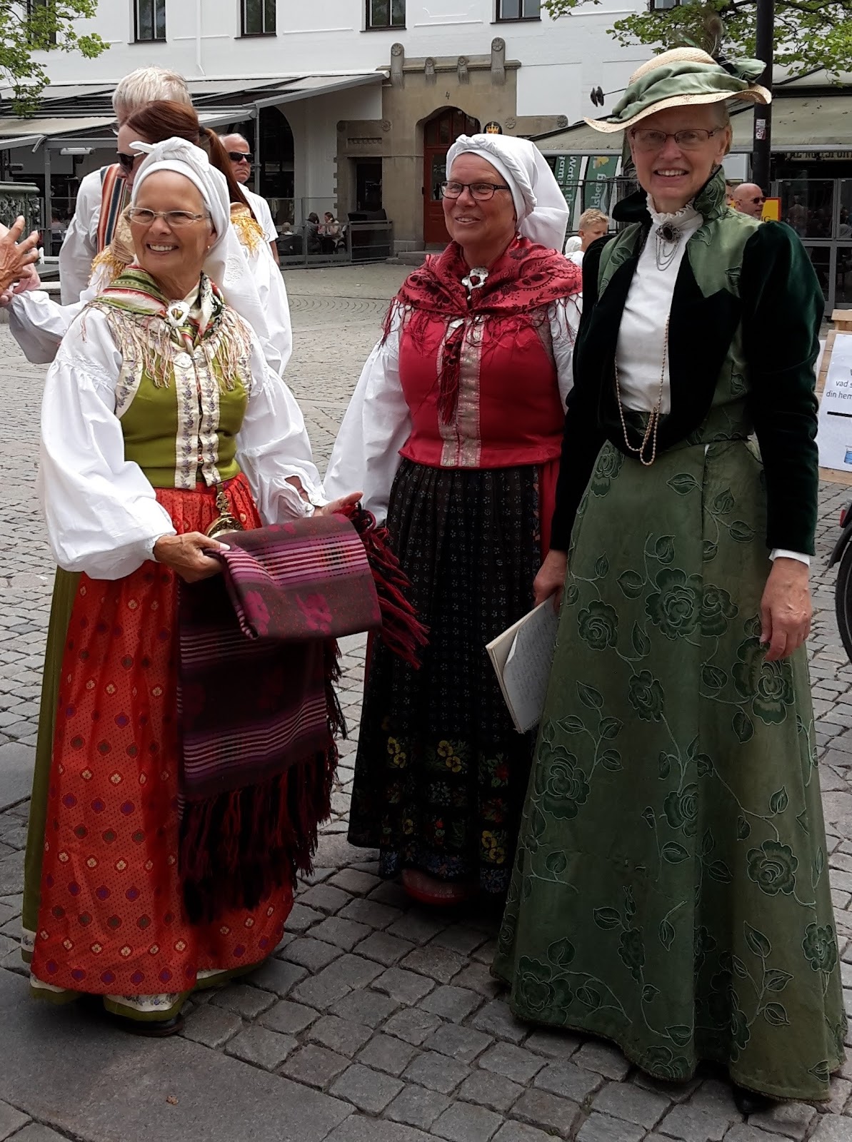 Dräktparad på Larmtorget i Kalmar. Mary har lånat sin dotters Möredräkt i grönt halvsiden med sidenförkläde. Irma bär Möredräkt i rött halvsiden med tryckt linneförkläde. Bredvid står Agneta.