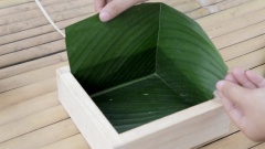Cách làm bánh chưng xanh: 4 lá dong cho 1 cái bánh chưng. Đầu tiên bạn đặt 1 sợi dây lạt bên dưới khuôn, tiếp theo xếp lá dong thứ nhất vào 1 góc của khuôn, dùng tay ấn 1 mặt lá xuống đáy khuôn sau đó gấp chéo để tạo hình đẹp cho mặt ngoài của bánh chưng. Lá dong thứ 2 xếp vào góc đối diện lá thứ nhất, không cần gấp chéo. Lá thứ 3 và 4 được xếp lần lượt vào 2 góc còn lại. Lấy 4 phần ngọn của những lá đã cắt ra khi đo lá, chèn vào 4 góc. Lớp chèn này sẽ đứng giữa 2 lớp lá giúp bánh không bị vỡ góc khi luộc.