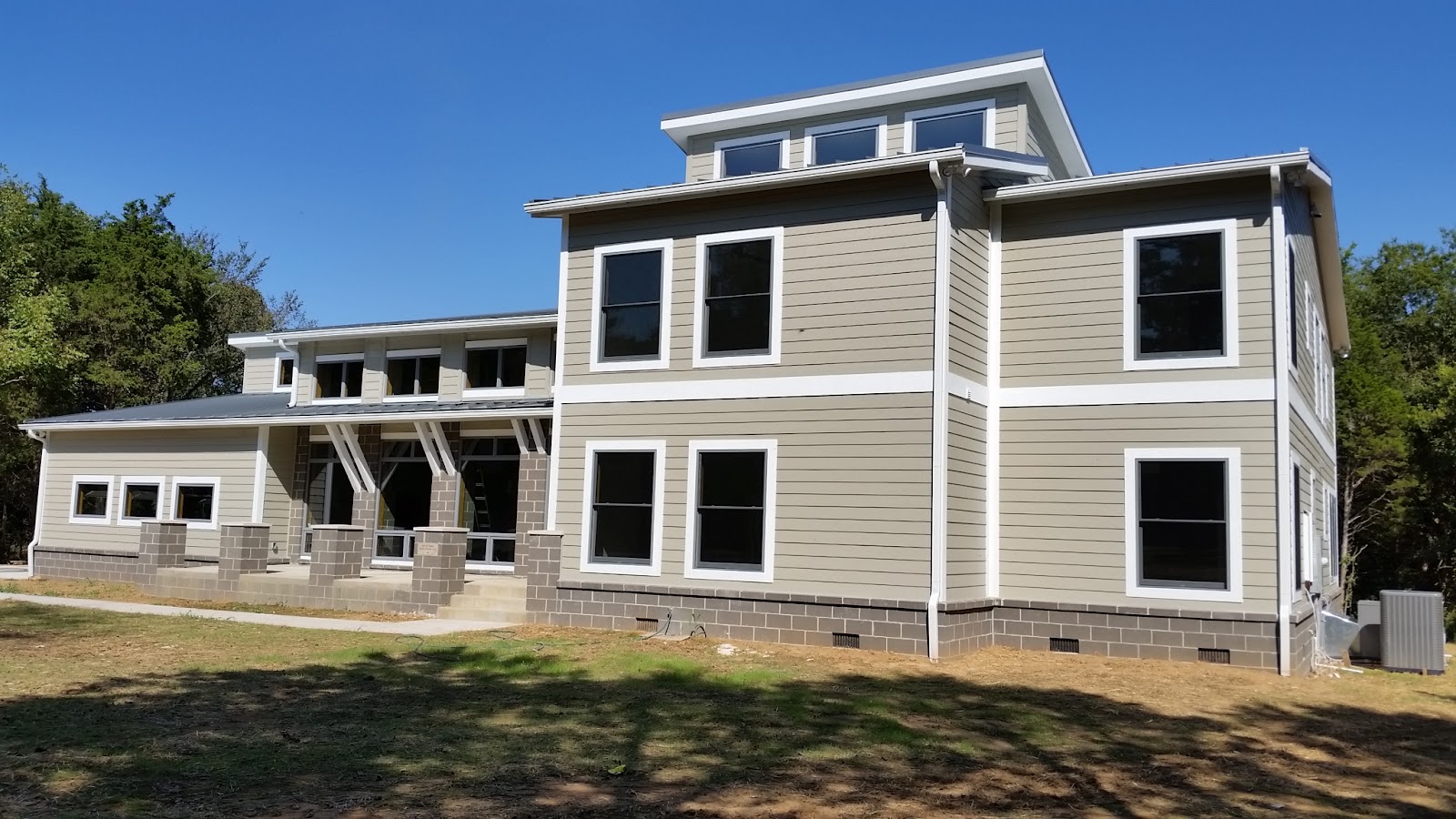 Exterior of a multi-story residential home with grey siding, white trim, and a block foundation.