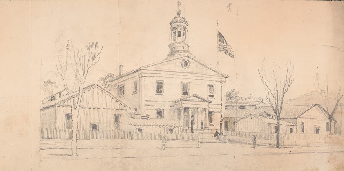 Courthouse or town hall surrounded by homes and outbuildings American flag flyin