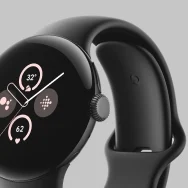 Google Pixel Watch 2 in Matte Black Aluminum Case / Obsidian Active Band. The watch face shows the time, weather, and heart rate. There also are icons for Fitbit and Google Assistant.