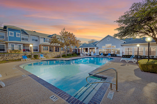 The Park at Summers Grove's swimming pool at dusk with sundeck featuring blue lounge chairs, next to clubhouse
