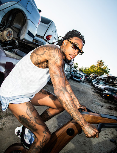 Wiz Khalifa riding a brown stationary exercise bike.