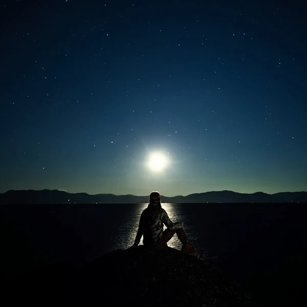 A photo of a person sitting on a rock before the ocean. The setting sun casts shadows across the landscape, and the Pixel 8 Pro camera is able to deliver sharp quality despite the low light.