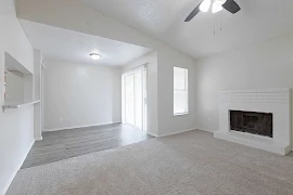 Bright, empty apartment interior with mixed floors, a fireplace, and sliding glass door leading to a balcony.