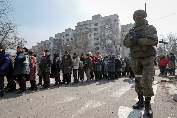 A Russian soldier stands near residents queuing for food delivered during Ukraine-Russia conflict, in the besieged southern port of Mariupol, Ukraine, March 23 2022. Picture: ALEXANDER ERMOCHENKO/REUTERS