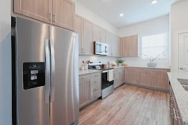 Modern kitchen with stainless steel appliances, wooden cabinets, and light countertops.