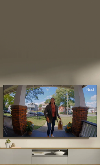 A TV in a living room showing a delivery person standing on a stoop waving to the doorbell camera.