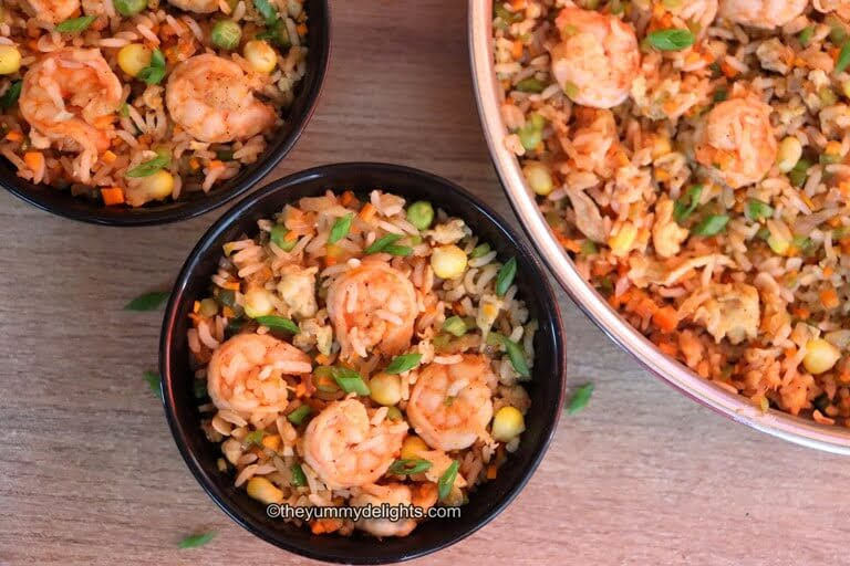 top view of shrimp fried rice served in two black bowls and a skillet with fried rice on the side.