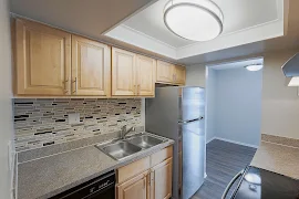 Kitchen with light wood cabinets, stone-inspired countertop, tile backsplash, and wood plank floors