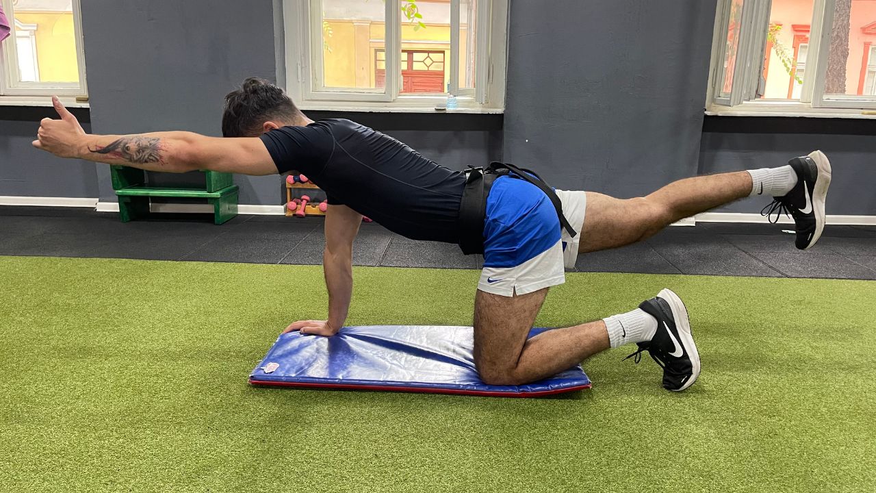 Vanja performs a bird dog exercise for the lower back in the commercial gym setup.