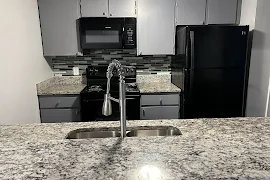 Kitchen with gray cabinets, black appliances, and stone countertops 