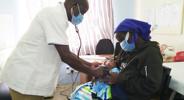 A medic examines a baby before circumcision in a health facility in Nyanza.