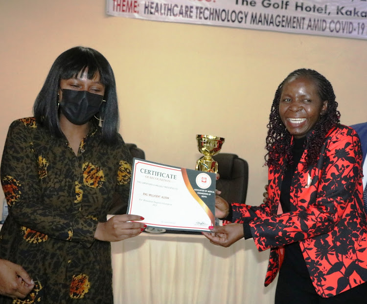 Health Cabinet Administrative Secretary Mercy Mwangangi presents a trophy and certificate to AMKE secretary general Millicent Alooh during the association's 12th scientific conference at Golf Hotel in Kakamega on Wednesday