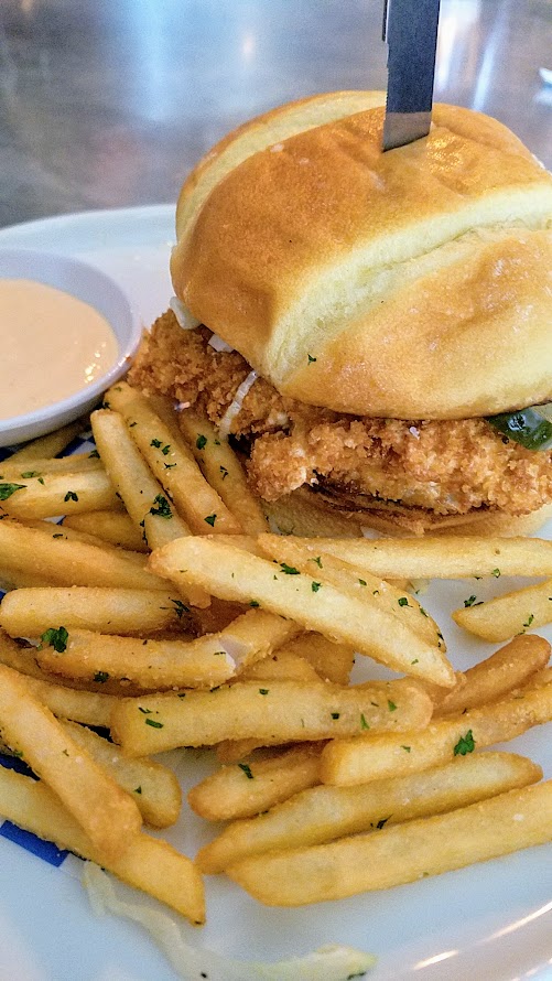 Shipwreck PDX food dish of Chicken Fried Fish Sandwich with tartar sauce, pickles, lettuce, potato bun, fast food fries, spicy dipping sauce