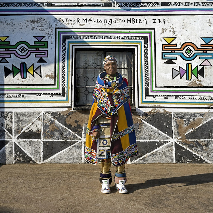 Dr Esther Mahlangu poses in front of an abode she has adorned with her distinctive interpretation of Ndebele visual traditions.