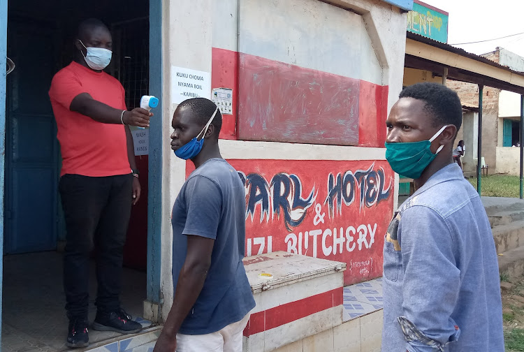 A restaurant attendant takes the temperature of a client before allowing him in in Amagoro, near Malaba town.