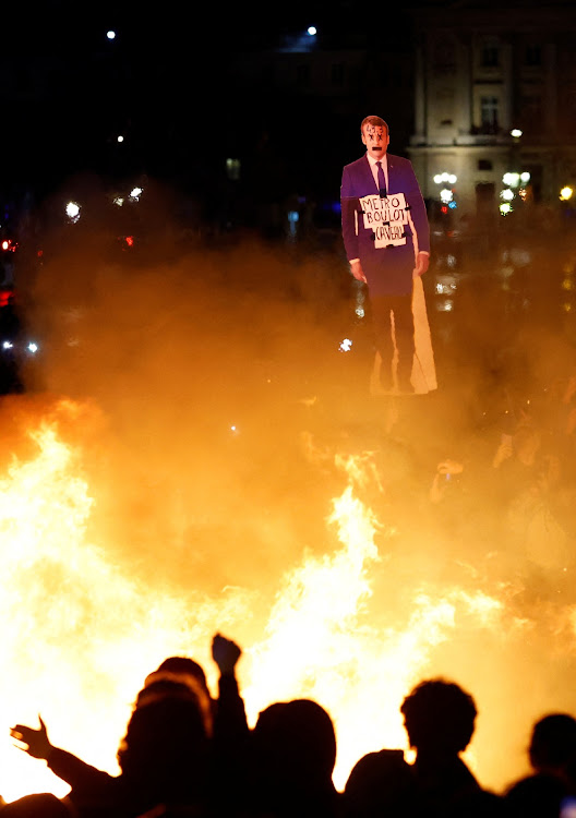 A protester holds a cut-out depicting French President Emmanuel Macron near a fire during a demonstration against France's pensions reform bill.