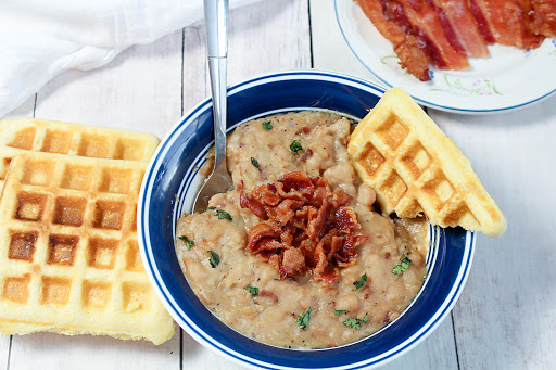 A bowl of bean & bacon soup with cornbread waffles and crumbled bacon on top.