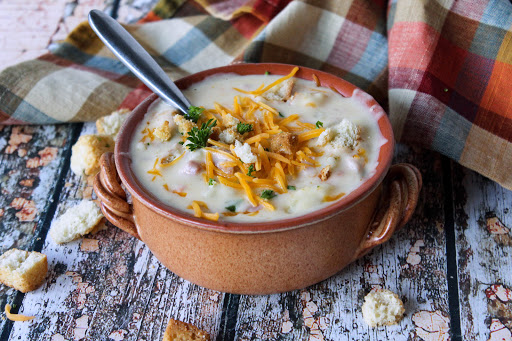 A bowl of potato soup with ham topped with croutons and cheddar cheese.