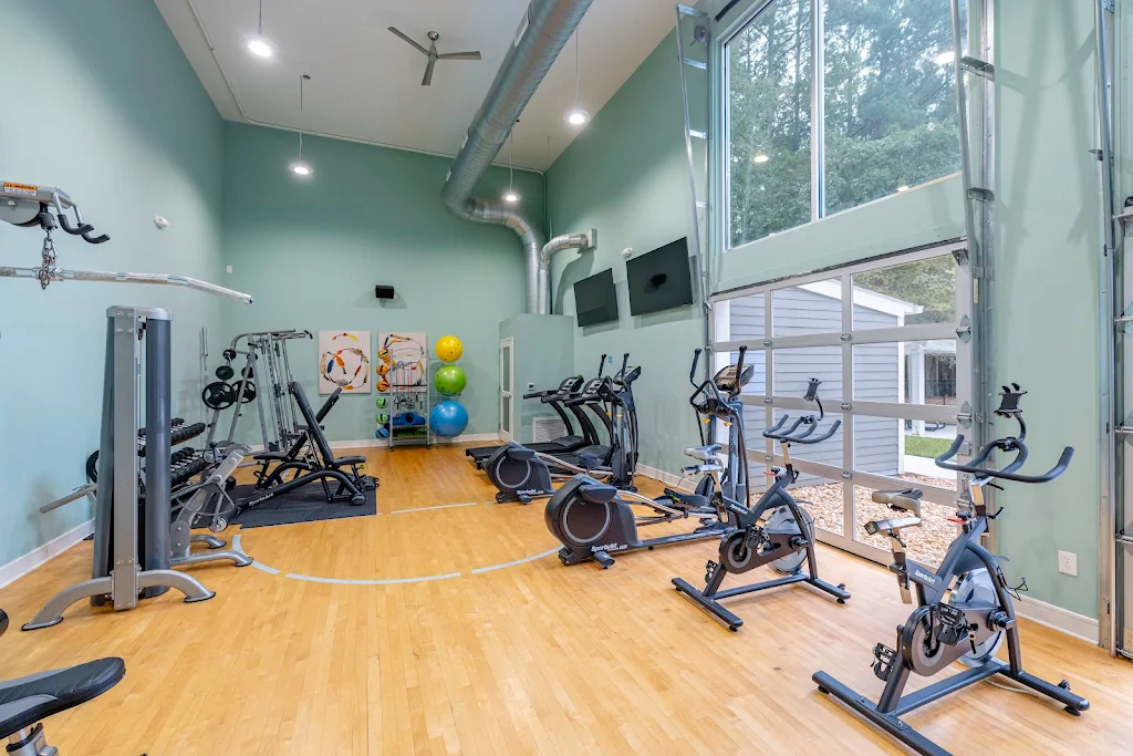 Community fitness center with high ceilings, gym flooring and various cardio and fitness machines.