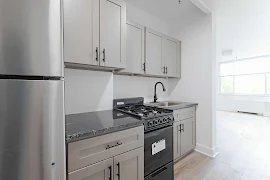 Modern kitchen with stainless steel appliances, gray cabinets, and granite countertops in a bright apartment.