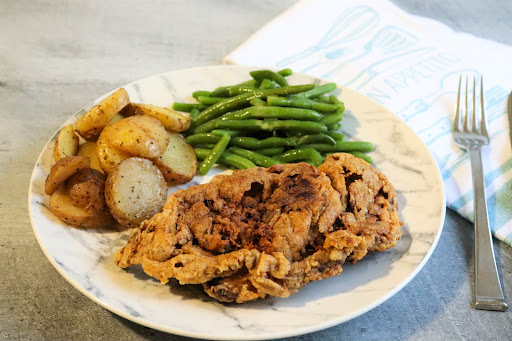 Chicken Fried Steak on a plate with potatoes and green beans.