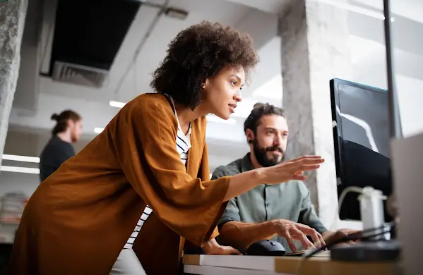 Teammates working together at a desk while looking at a computer