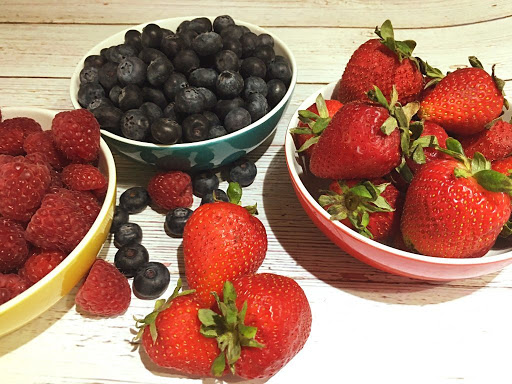 Strawberries, raspberries and blueberries sitting in bowls.