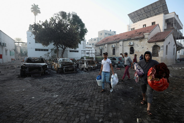 People walk with their belongings in the area of Al-Ahli hospital where hundreds of Palestinians were killed in a blast that Israeli and Palestinian officials blamed on each other, and where Palestinians who fled their homes were sheltering amid the ongoing conflict with Israel, in Gaza City, October 18, 2023.